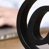 Uma fotografia de um sinal de internet @ na frente de alguém digitando em um laptop.