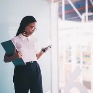Uma mulher em um escritório segurando um laptop e um celular.